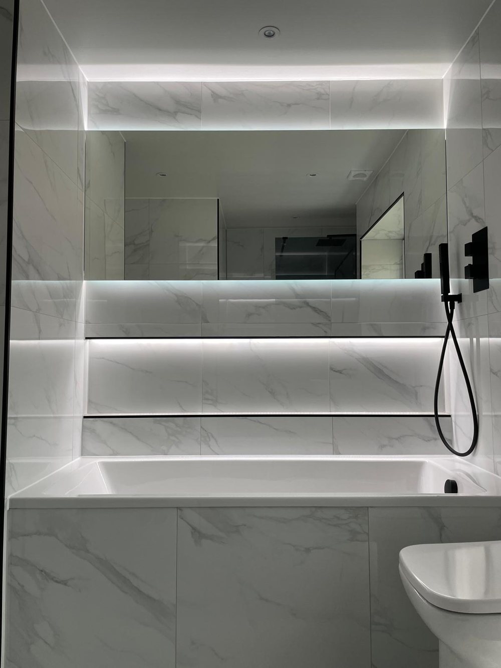 Bath with an LED lit shelf and black hand shower