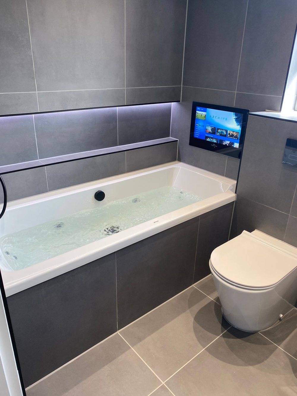 Bath with a TV set into a tiled niche