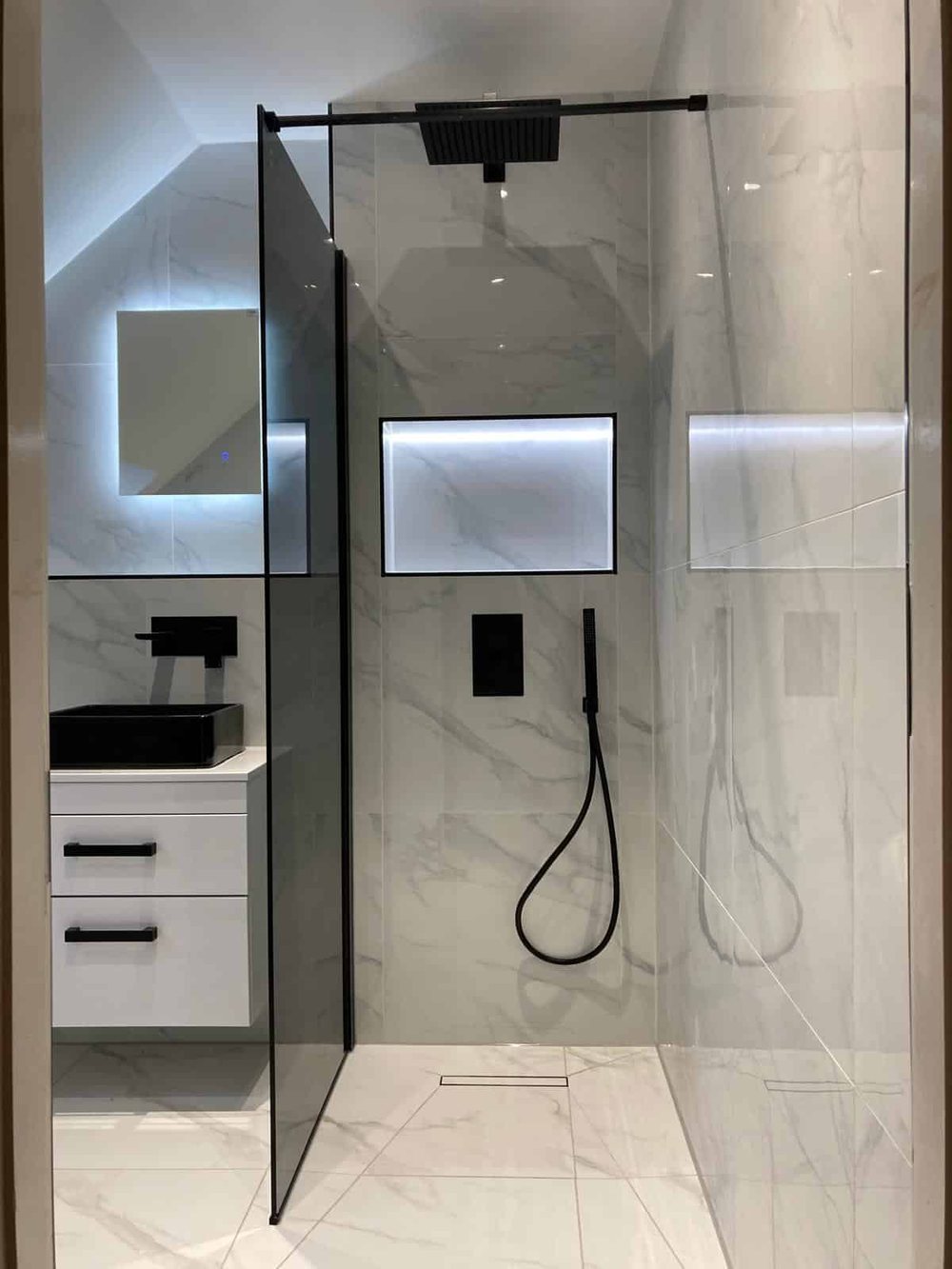 Black vessel basin on a white vanity with a lit shower niche